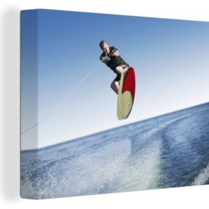 Canvas Schilderij Een man met een wetsuit is aan het wakeboarden op zee - 120x90 cm - Wanddecoratie
