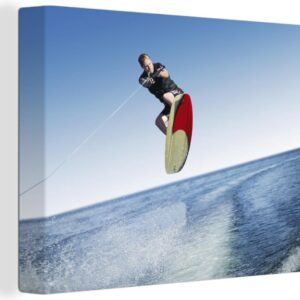 Canvas Schilderij Een man met een wetsuit is aan het wakeboarden op zee - 80x60 cm - Wanddecoratie